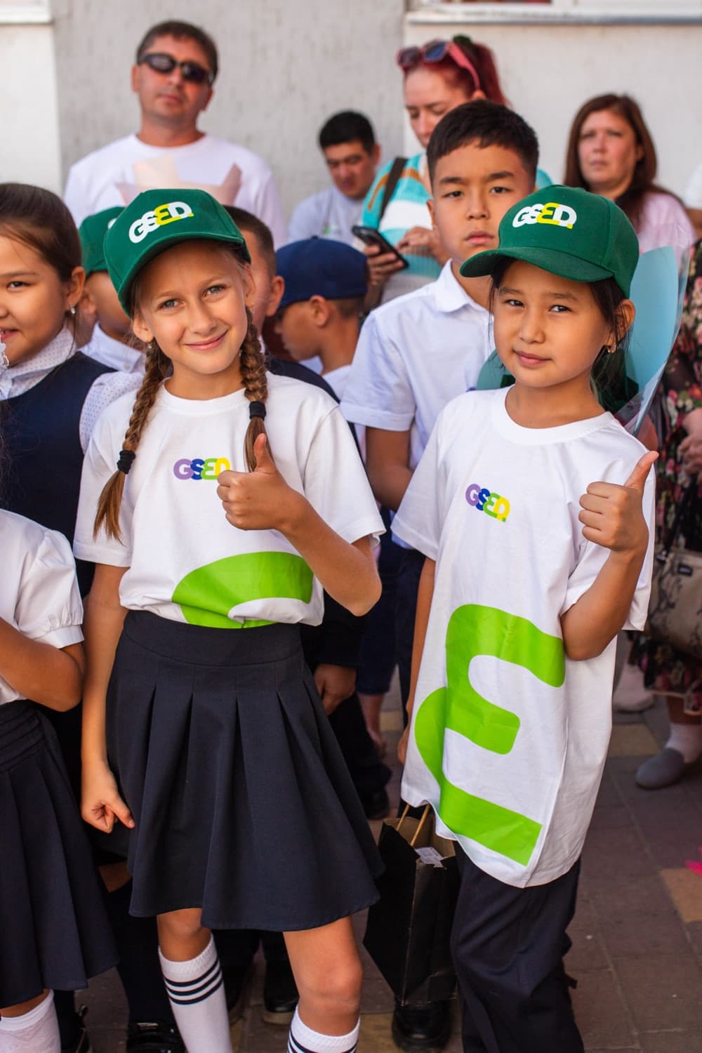 Two GSED students in branded caps giving a thumbs up